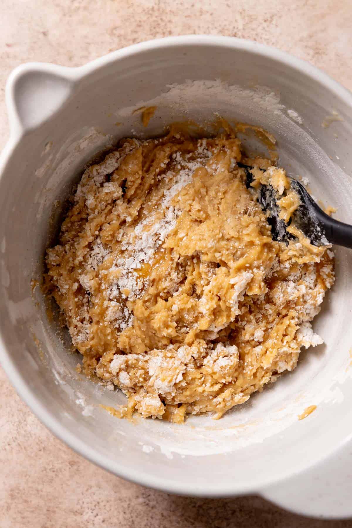 flour being folded into the cookie dough in a mixing bowl.