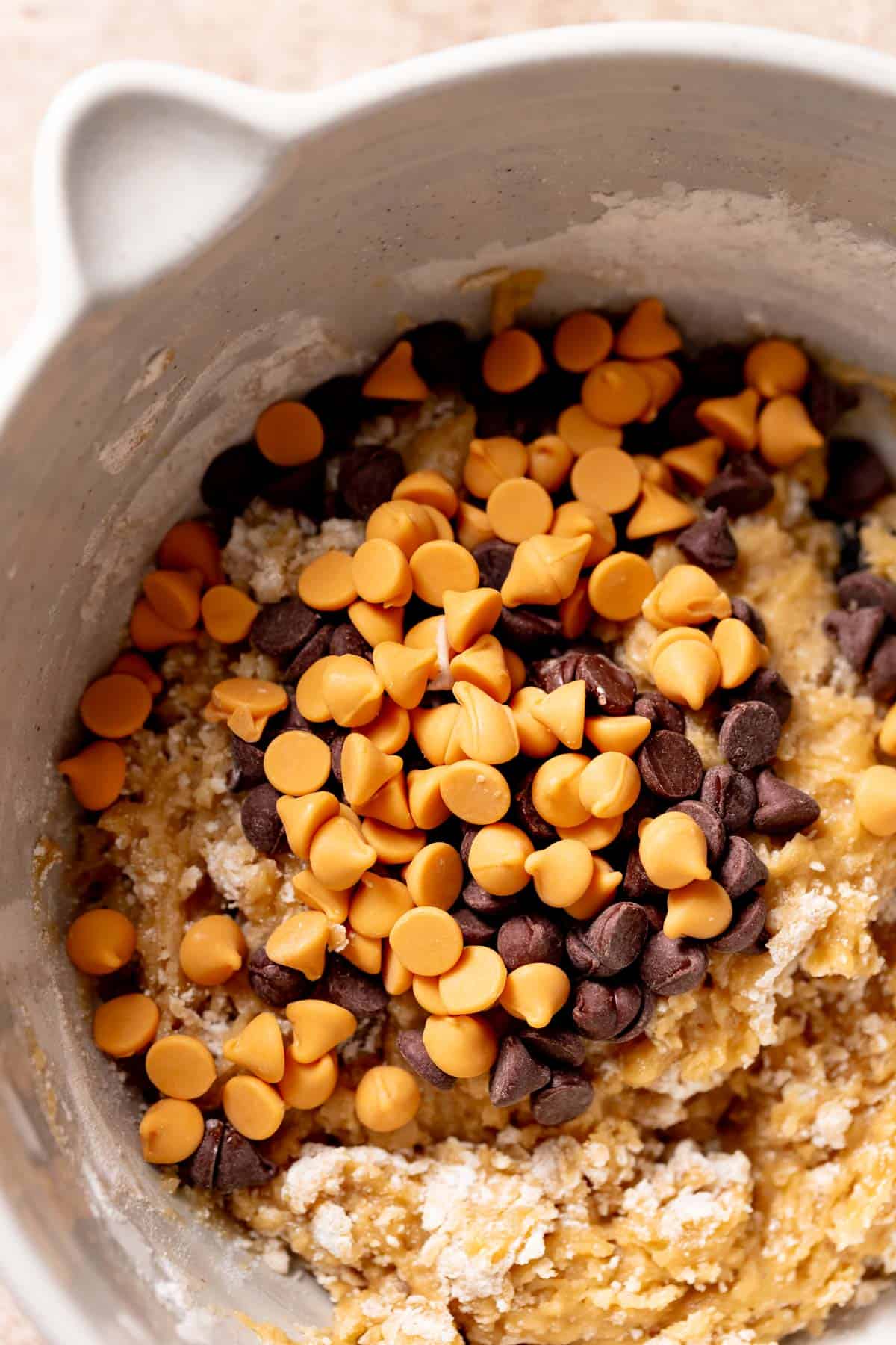 butterscotch chips and chocolate chips on top of the cookie dough in a bowl.