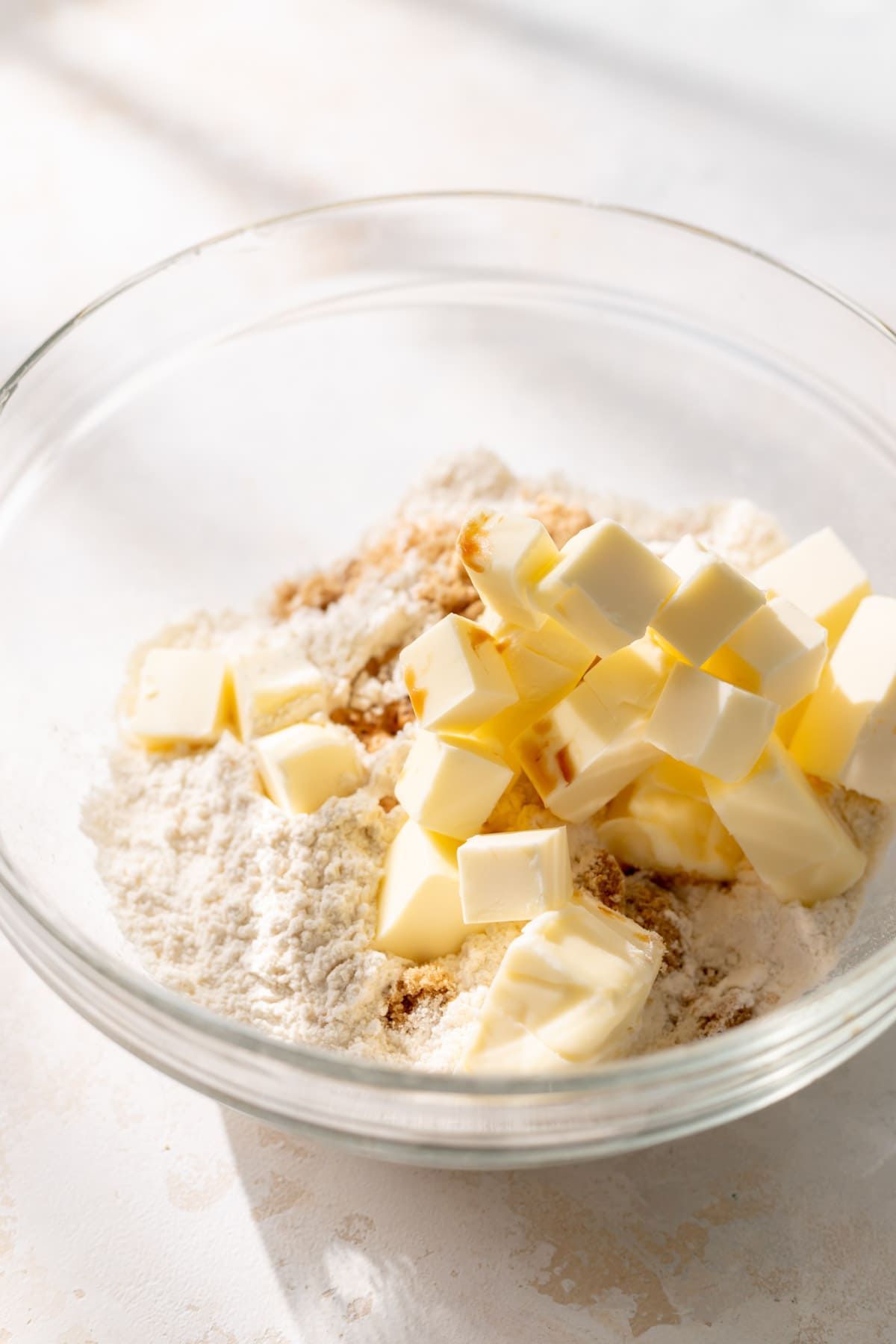 a glass bowl with cubed butter, sugar, and brown sugar before mixing.