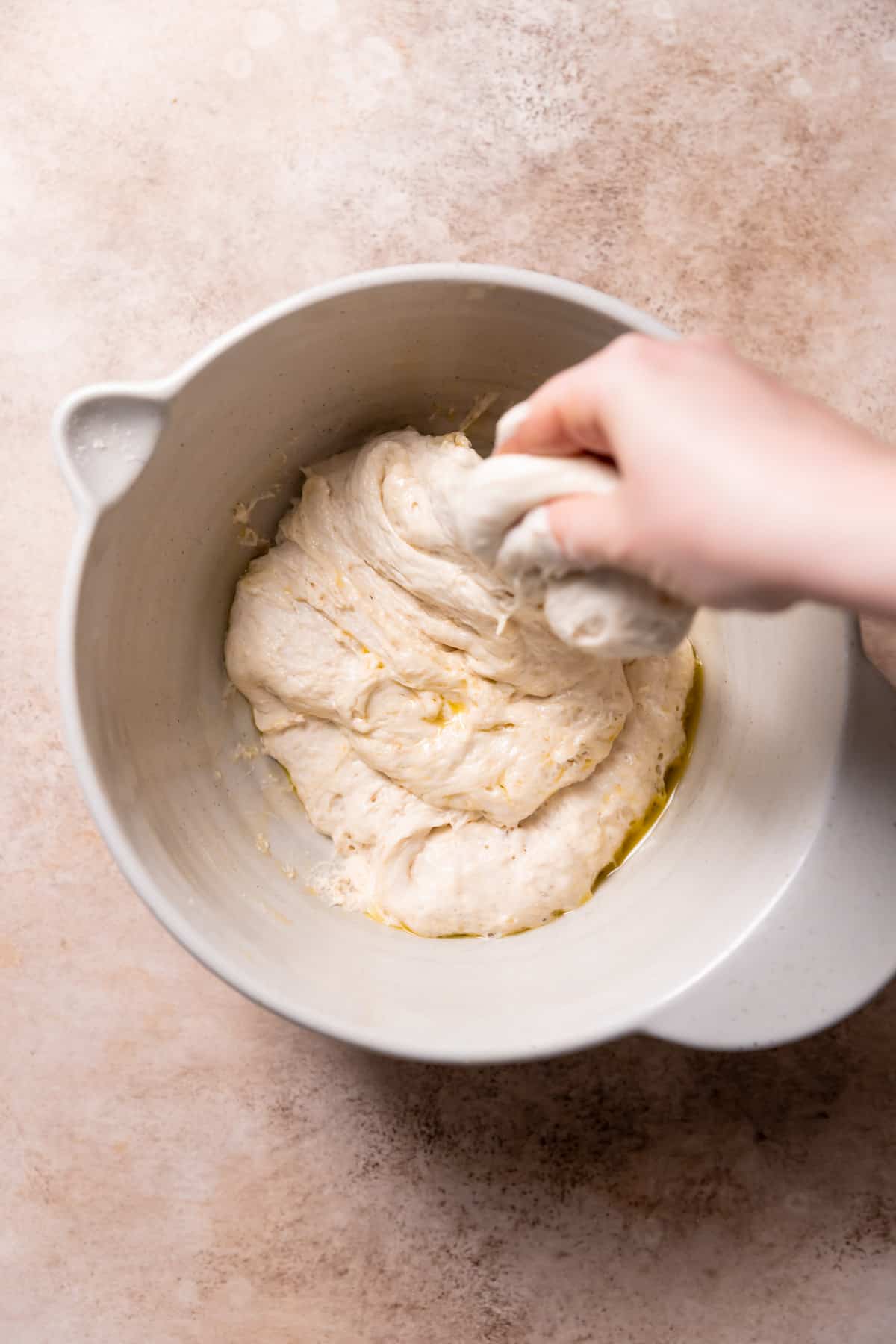 a hand stretching and folding the focaccia dough in a bowl.