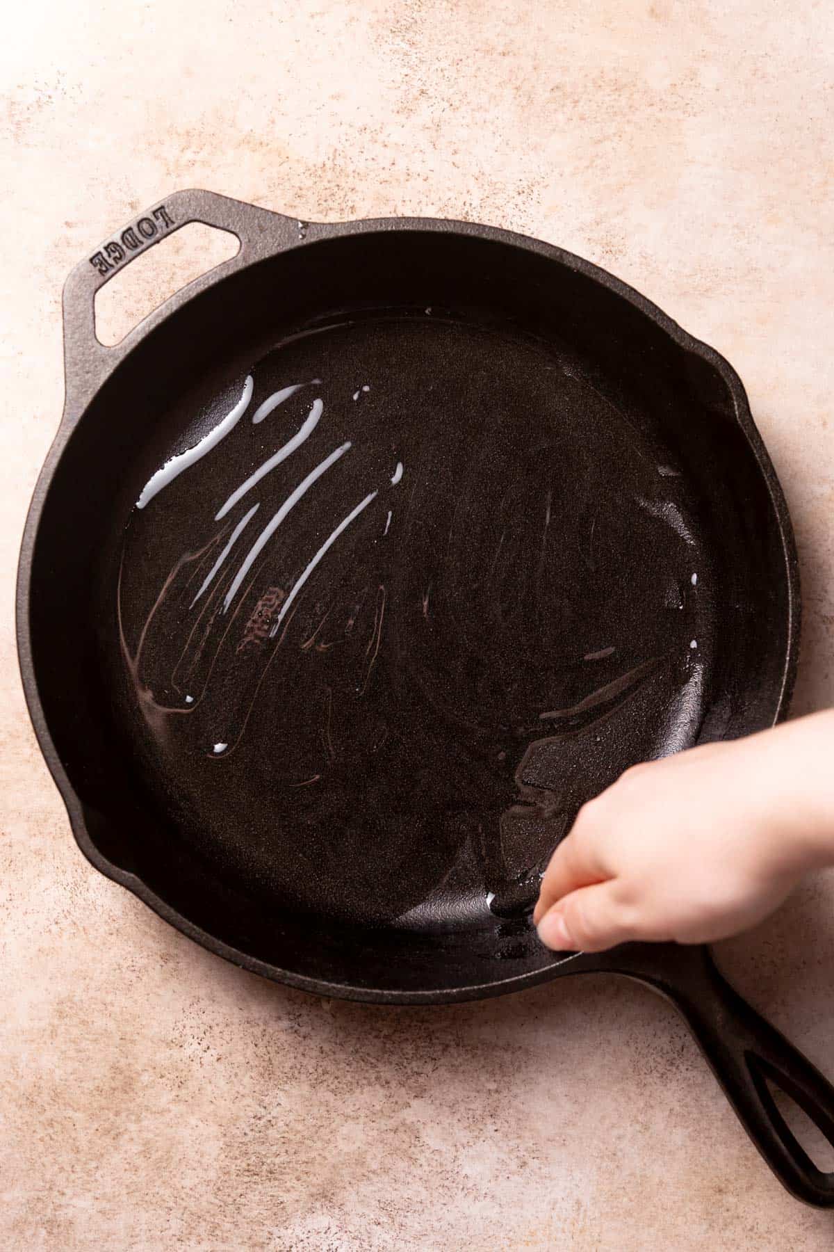 a hand rubbing olive oil on the cast iron pan.