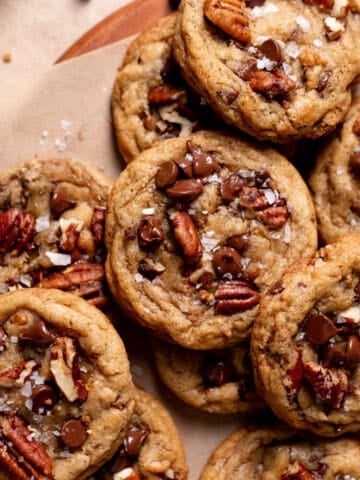 a pile of chocolate chip pecan cookies topped with chocolate chips and flaky sea salt.