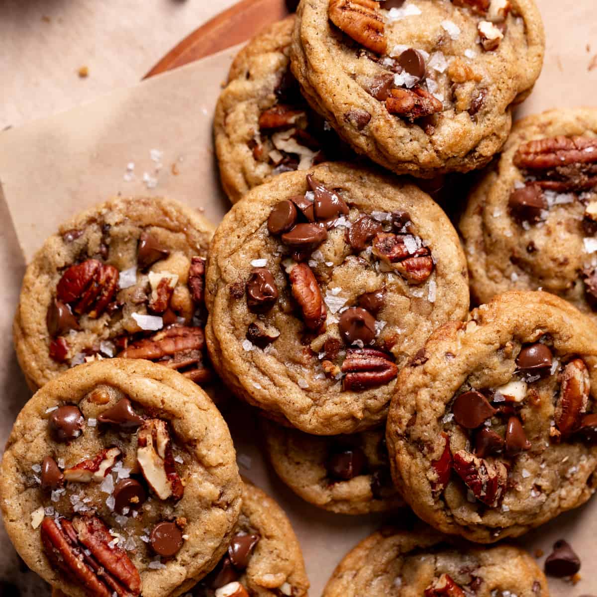 a pile of chocolate chip pecan cookies topped with chocolate chips and flaky sea salt.