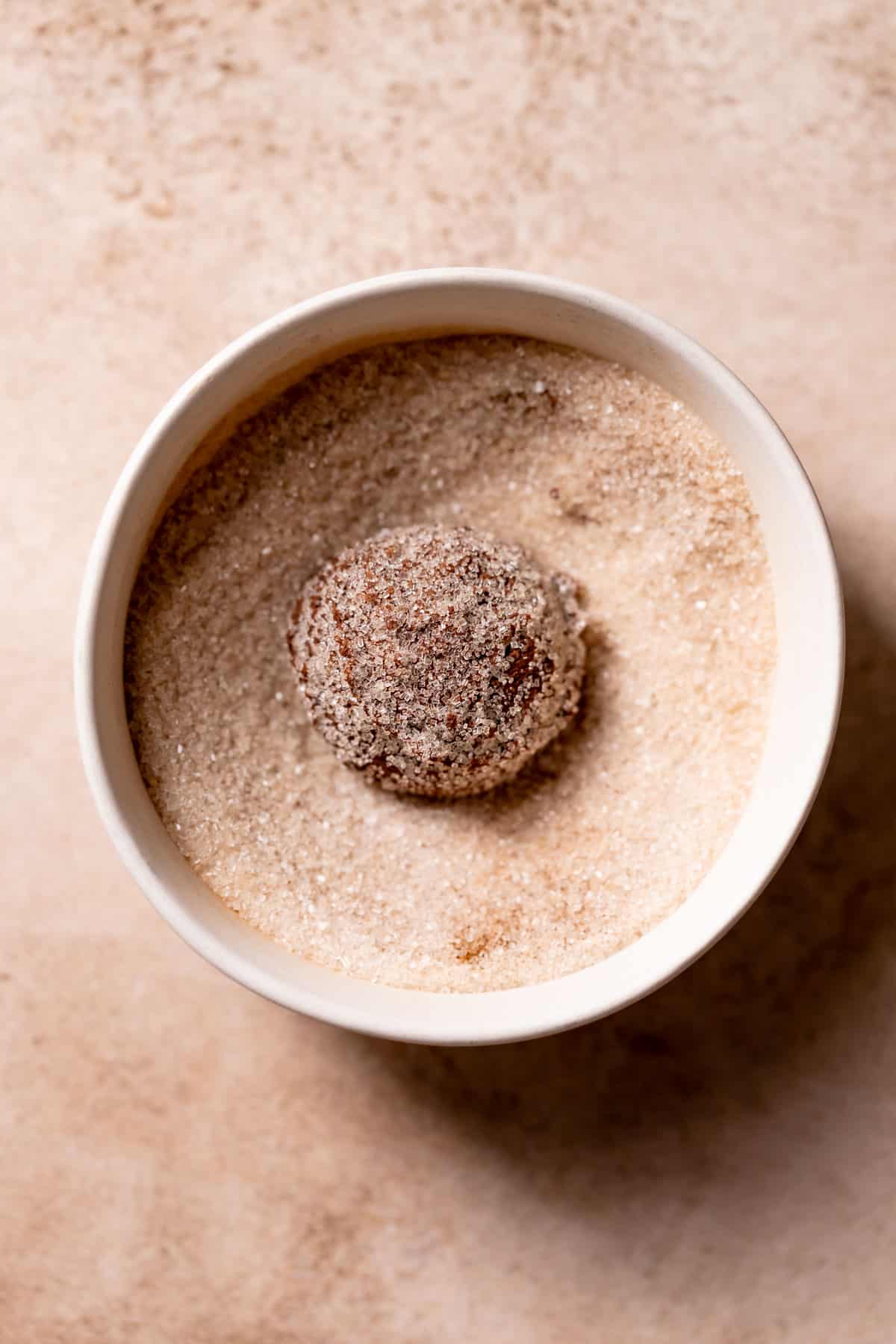 chocolate cookie dough ball in a bowl of cinnamon sugar.