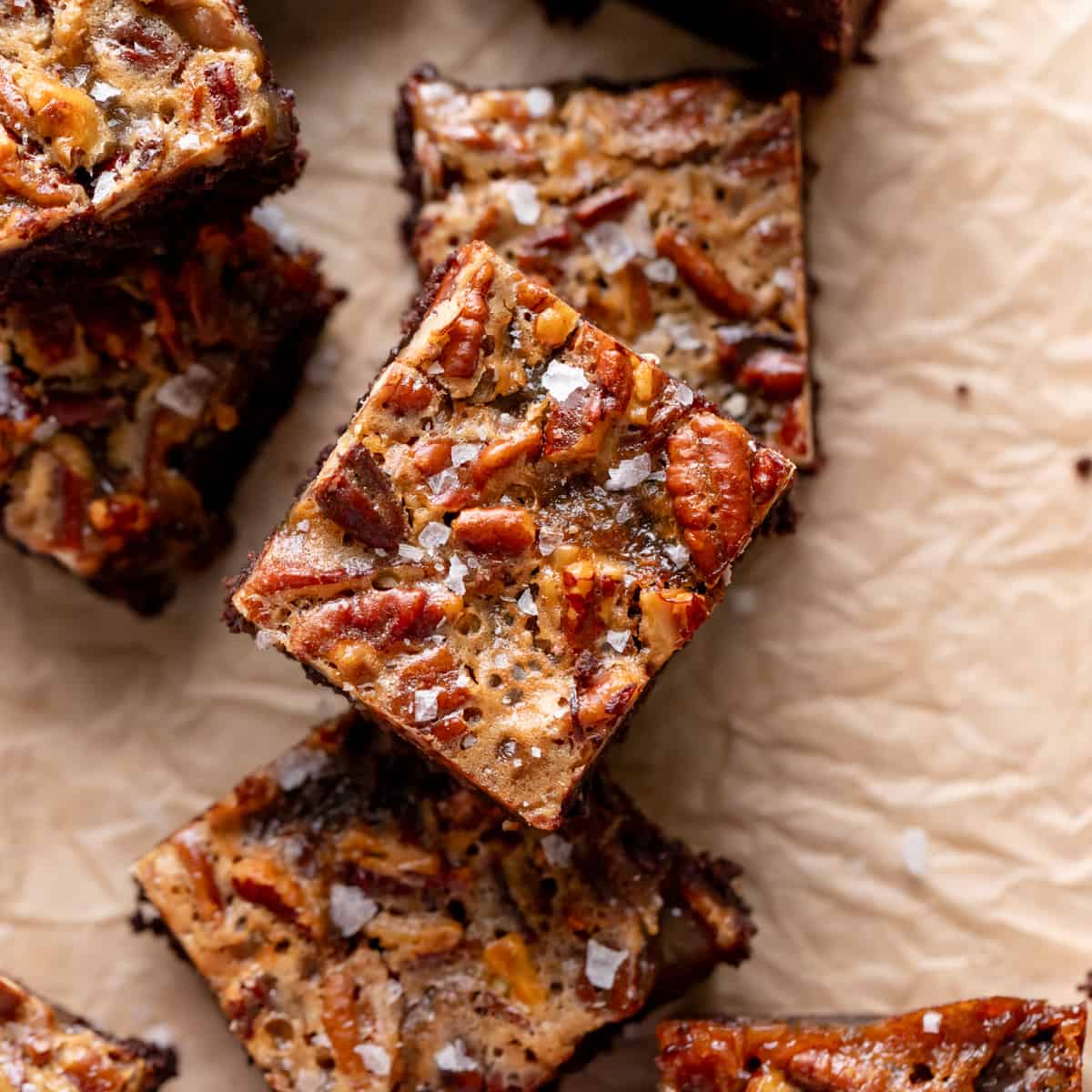 pecan pie brownies stacked on a piece of brown parchment paper.