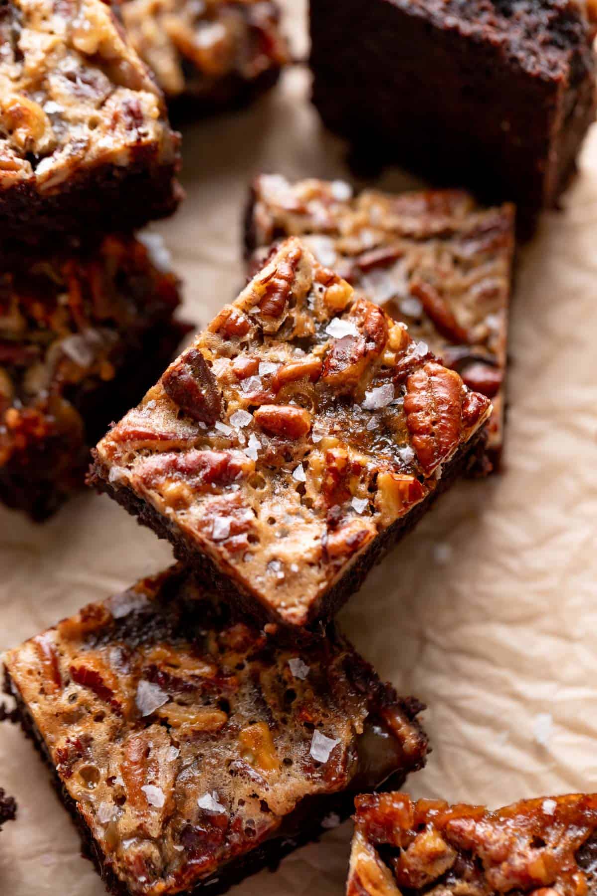 pecan pie brownies sprinkled with sea salt and stacked on top of each other on parchment paper.