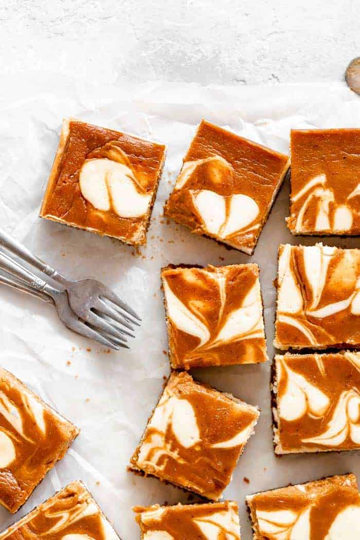 Pumpkin cheesecake bars on white parchment paper.