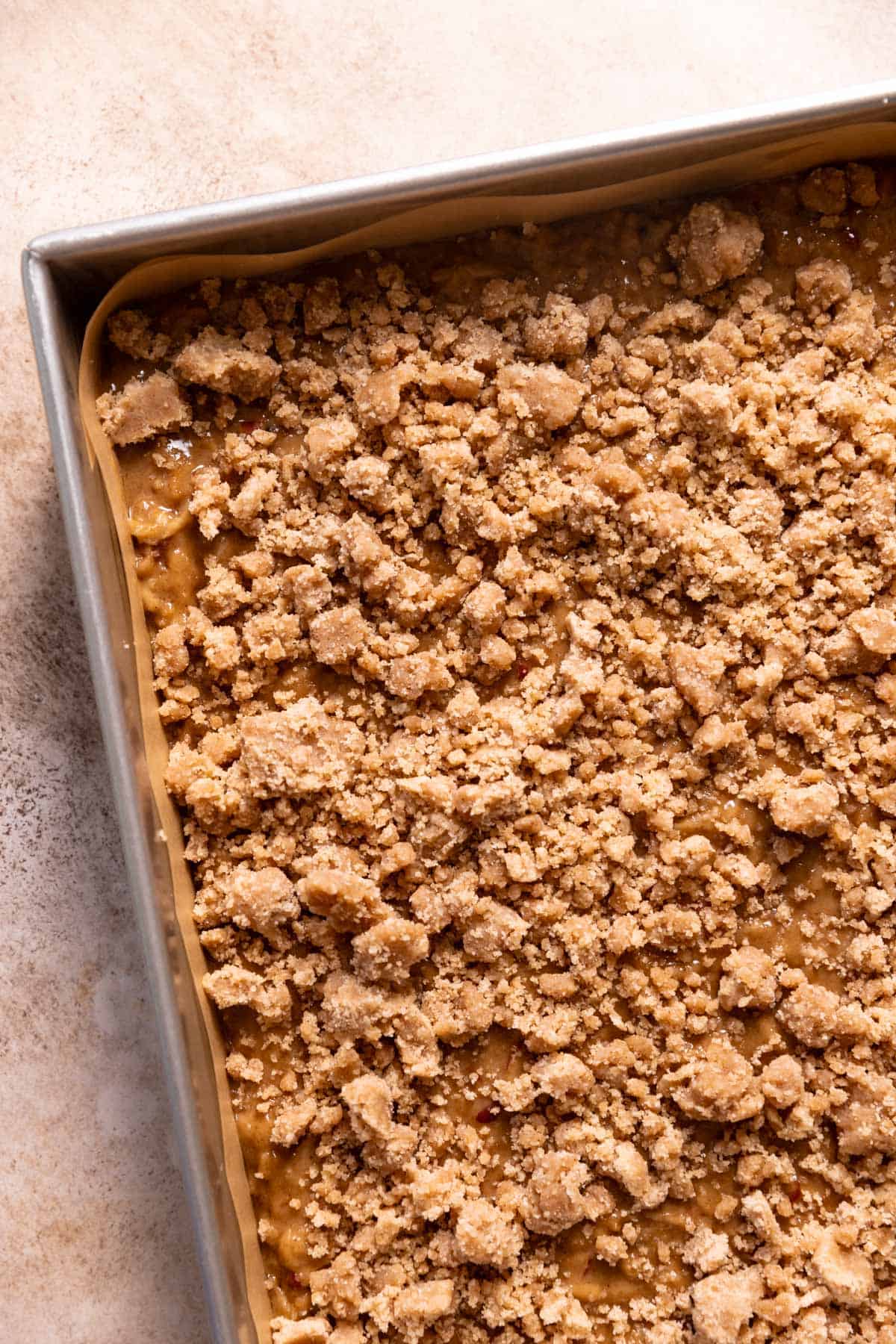 A baking pan with the apple cake batter and cinnamon crumbs on top before baking.