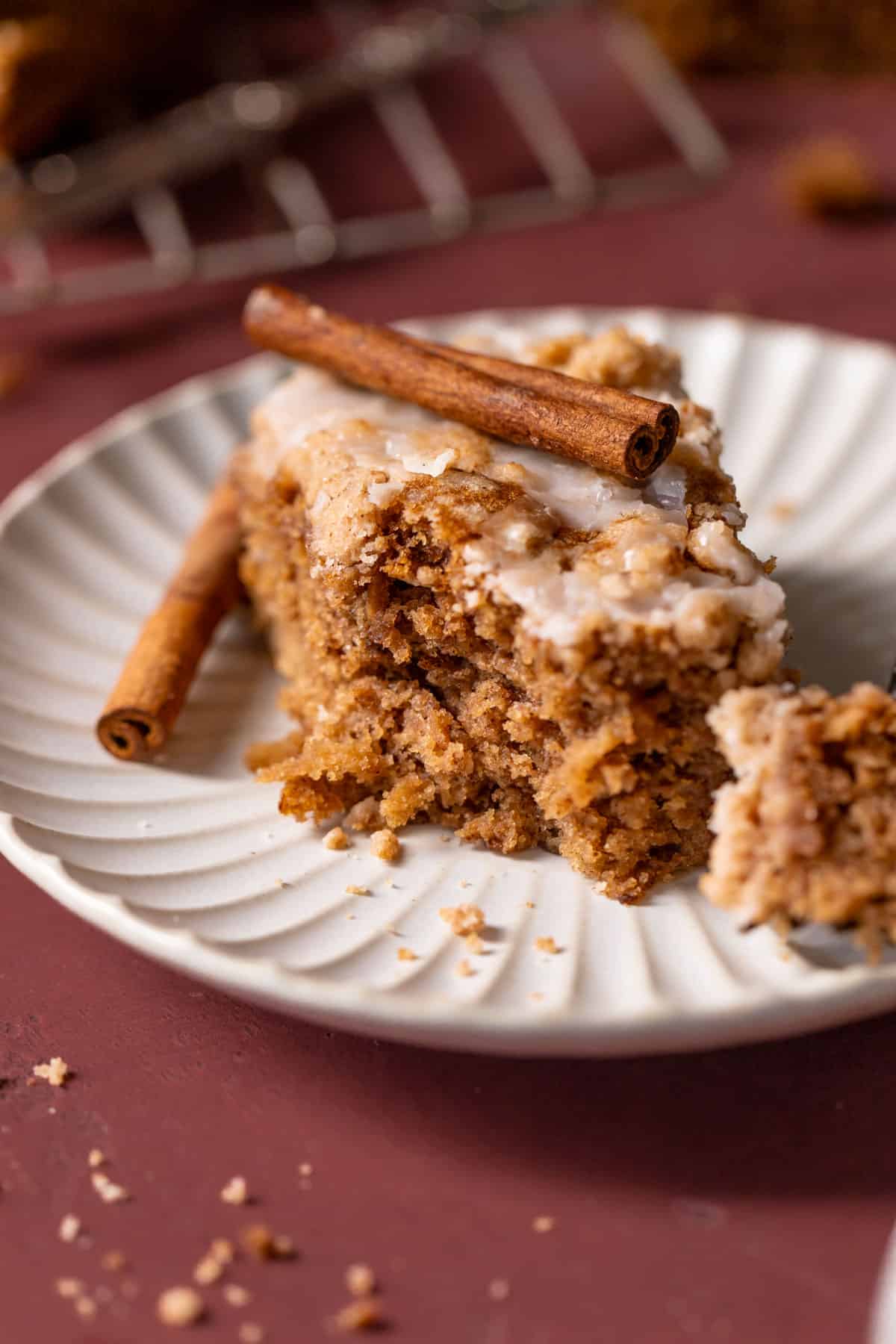 a slice of apple cake on a plate with a stick of cinnamon on top.