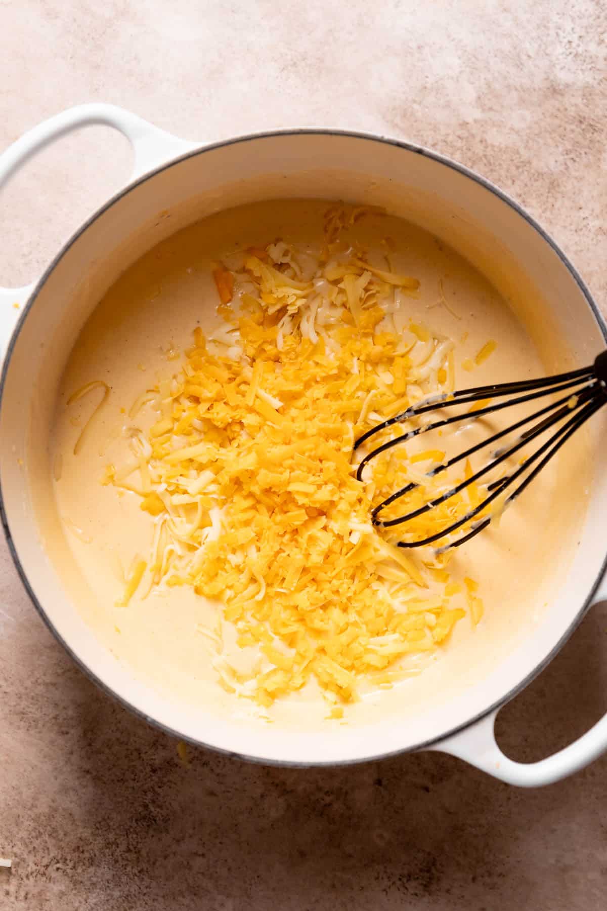 whisking the shredded cheeses into the sauce with a whisk.
