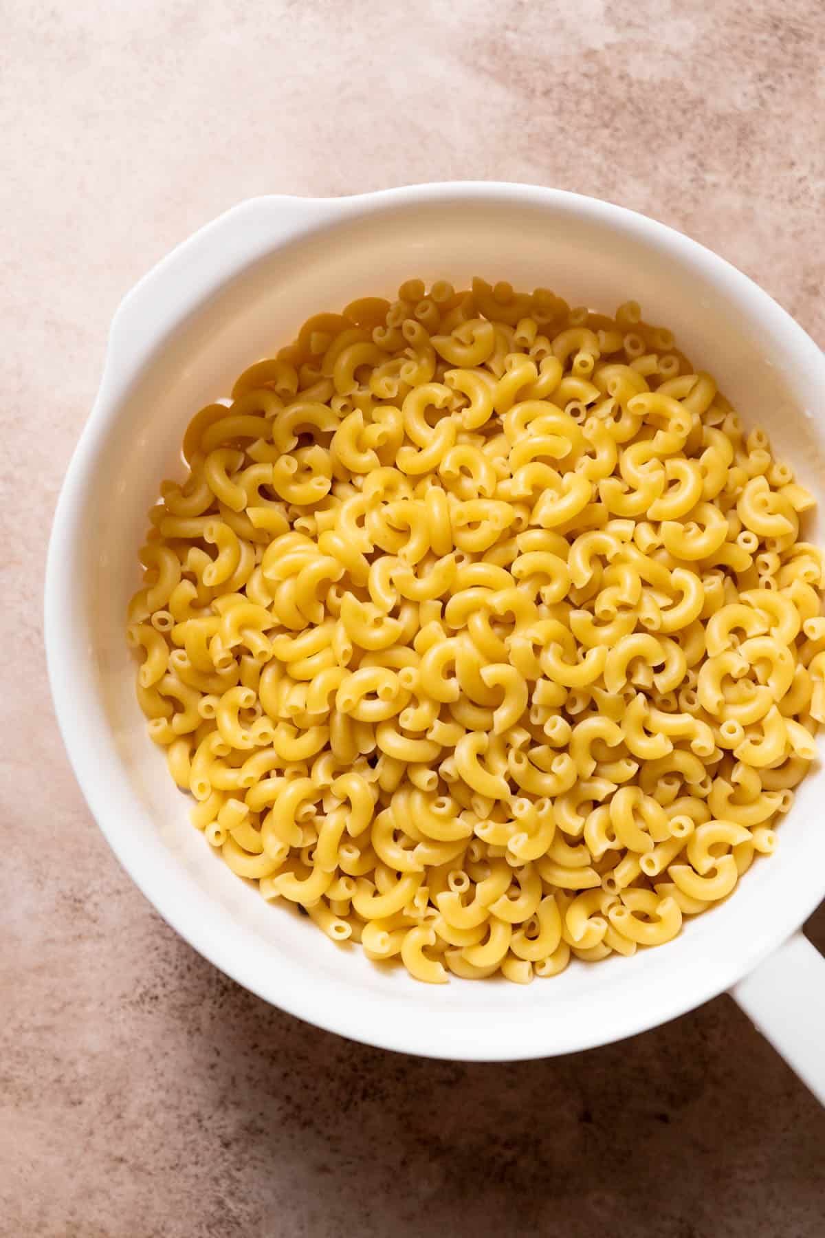 a colander full of cooked elbow macaroni noodles.