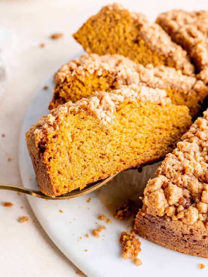 A slice of pumpkin coffee cake being pulled out from the whole cake.