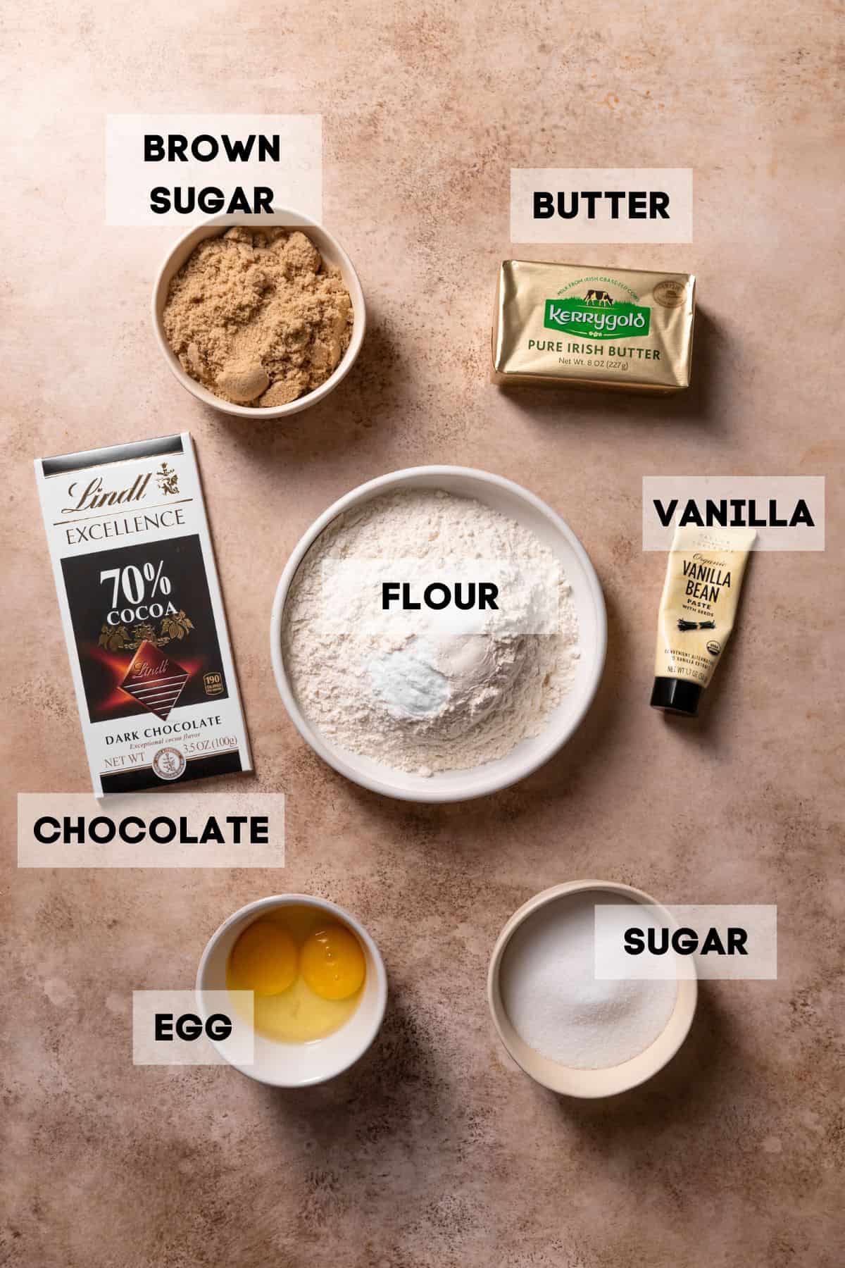 Ingredients needed to make chocolate chip cookies with toffee in bowls with labels.
