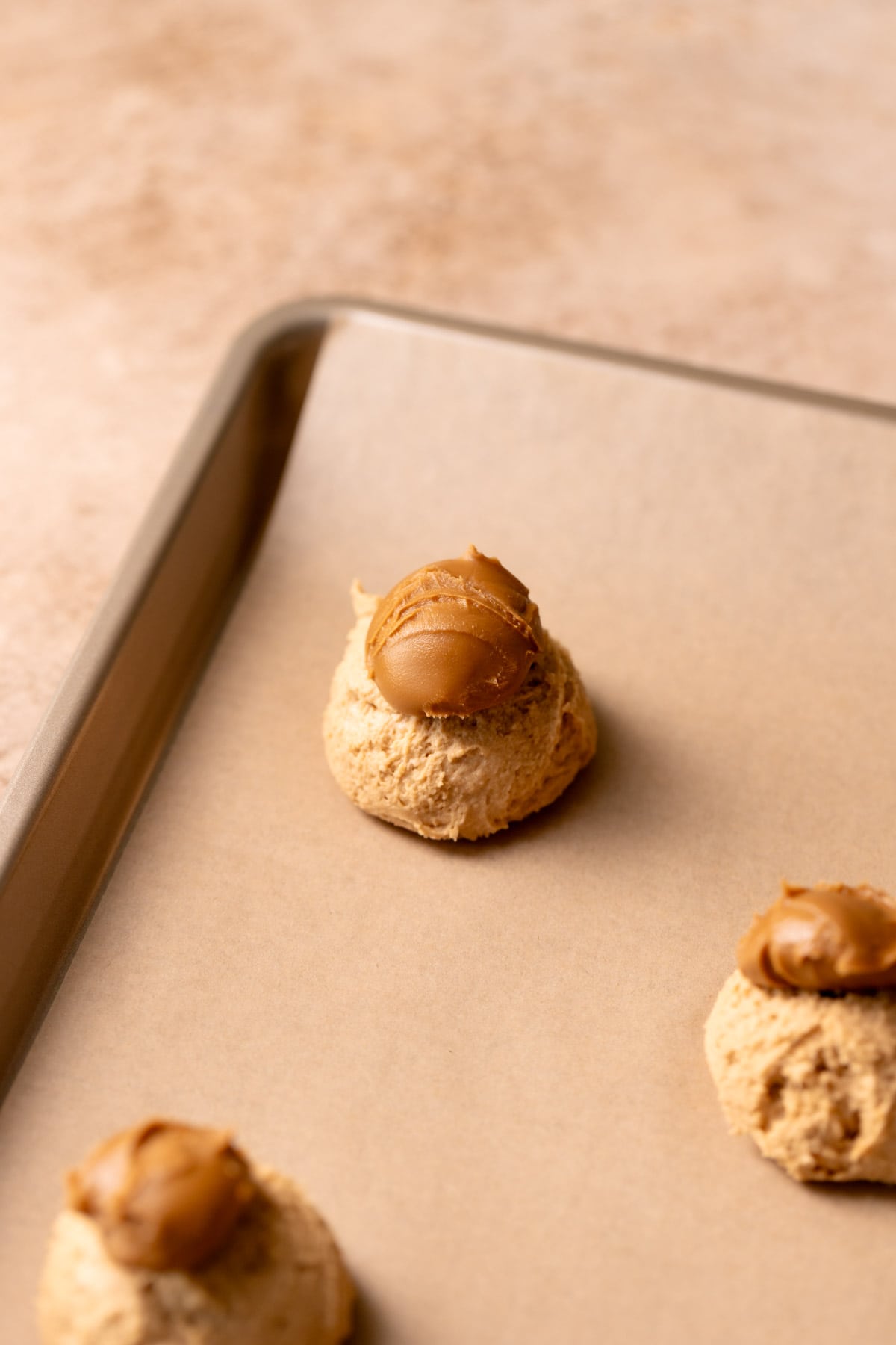 A cookie dough ball on a baking sheet with a glob of Biscoff cookie butter on top.