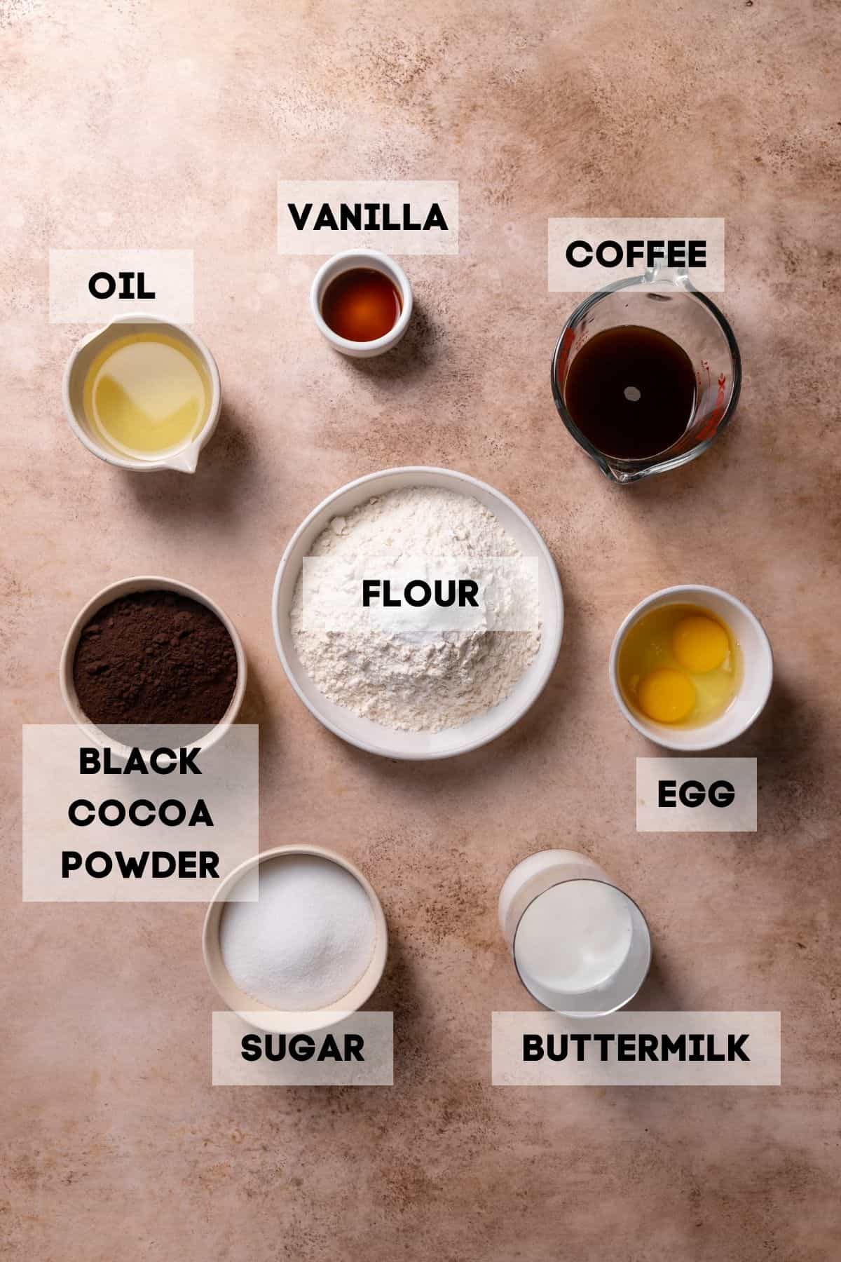 Ingredients needed to make black chocolate cake in bowls with labels.