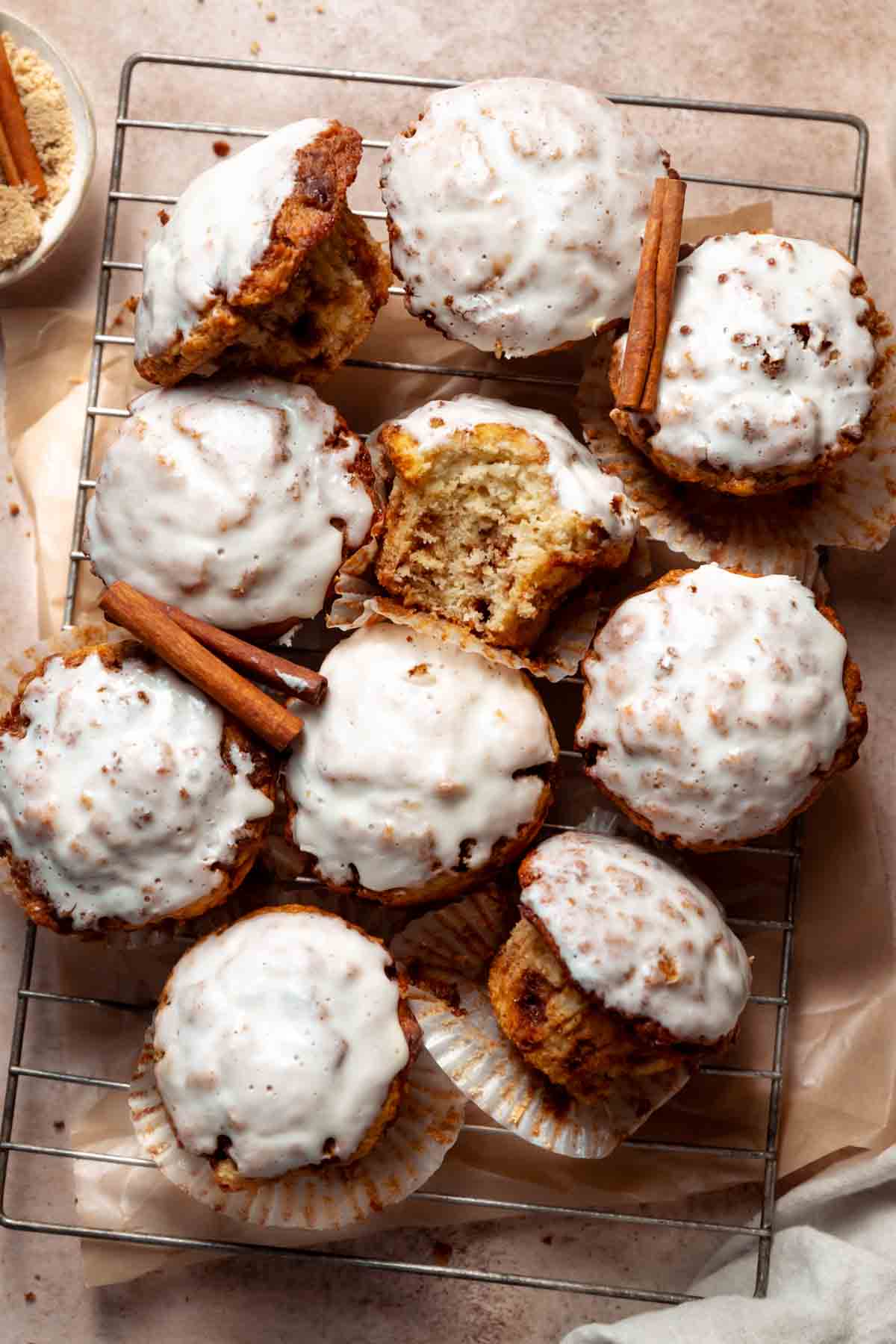 Cinnamon bun muffins covered in cream cheese icing on a wire cooling rack.