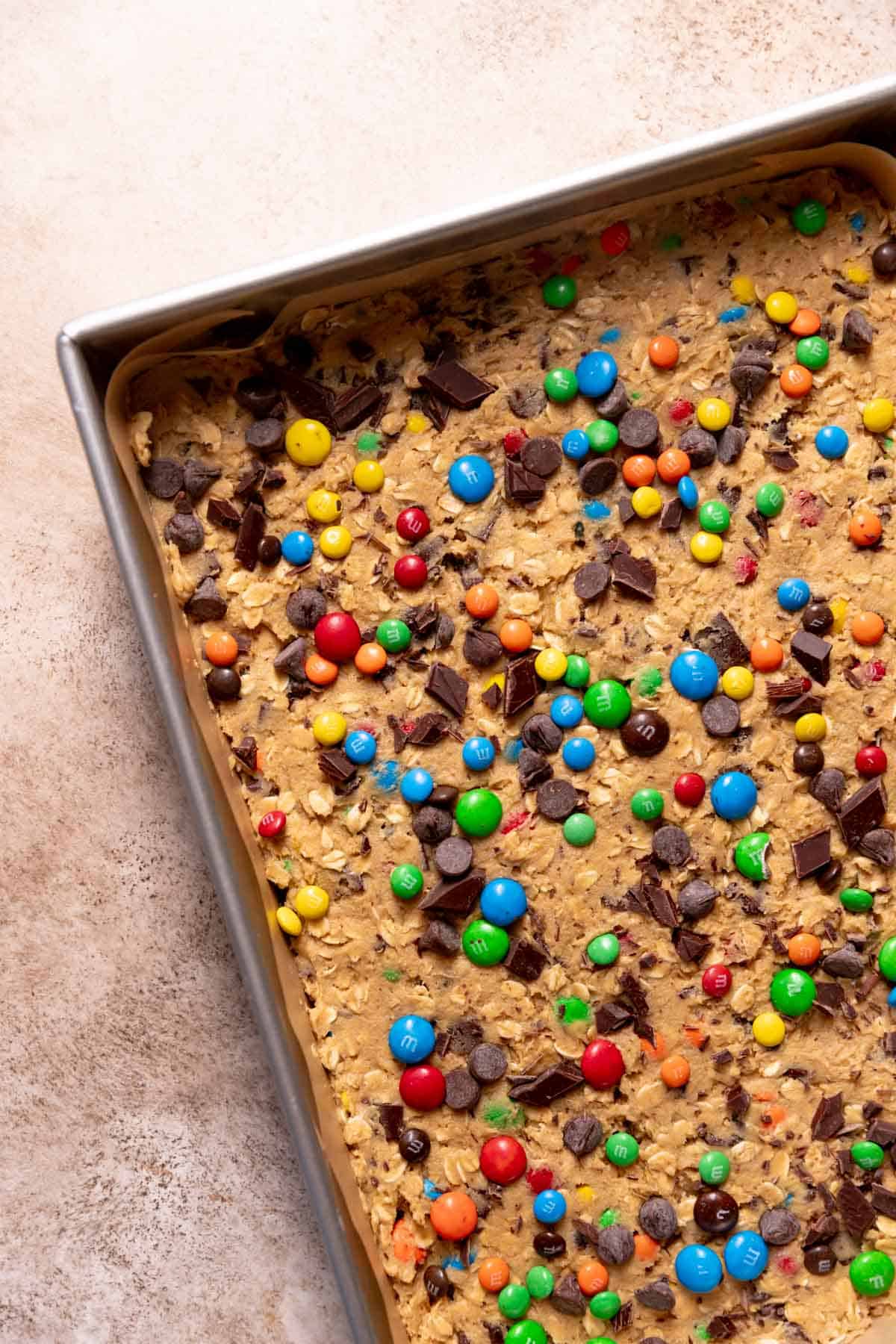 A baking pan with the peanut butter cookie dough pressed into the pan with extra candies and chocolate chips on top.