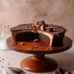 Reeses peanut butter cake on a wooden cake stand with slices missing to show the filling.