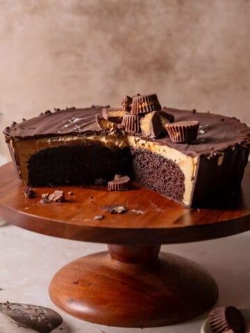 Reeses peanut butter cake on a wooden cake stand with slices missing to show the filling.
