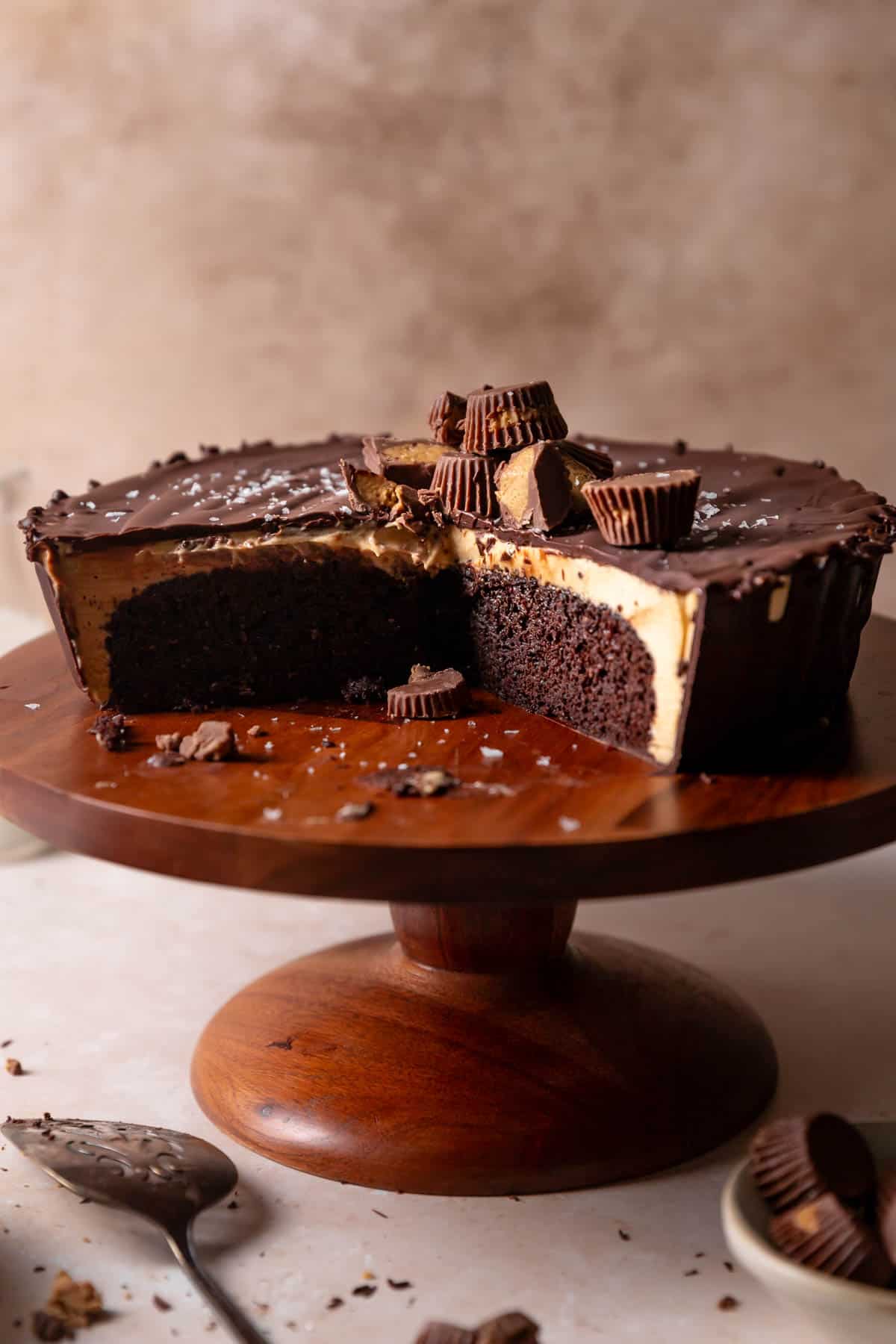 Reeses peanut butter cake on a wooden cake stand with some slices missing.