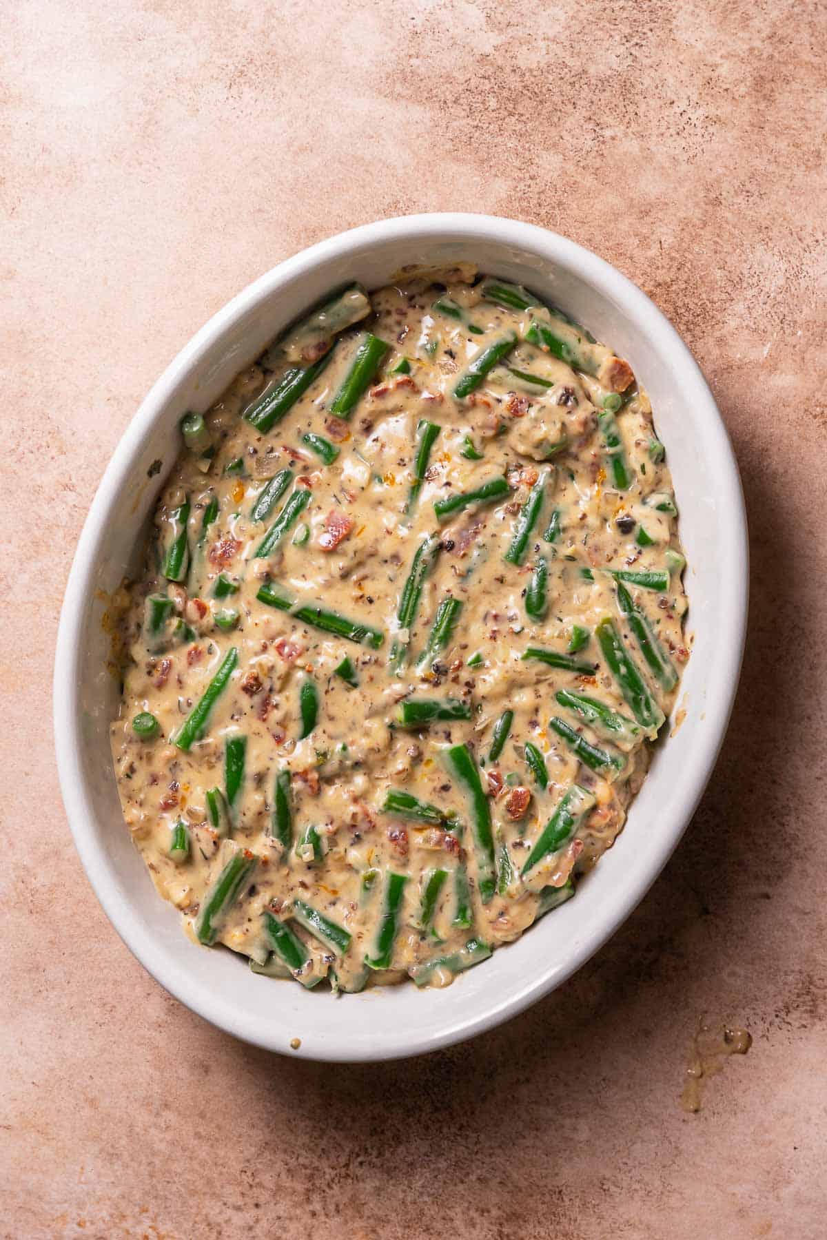 Cheesy green bean casserole in a white baking dish before baking.