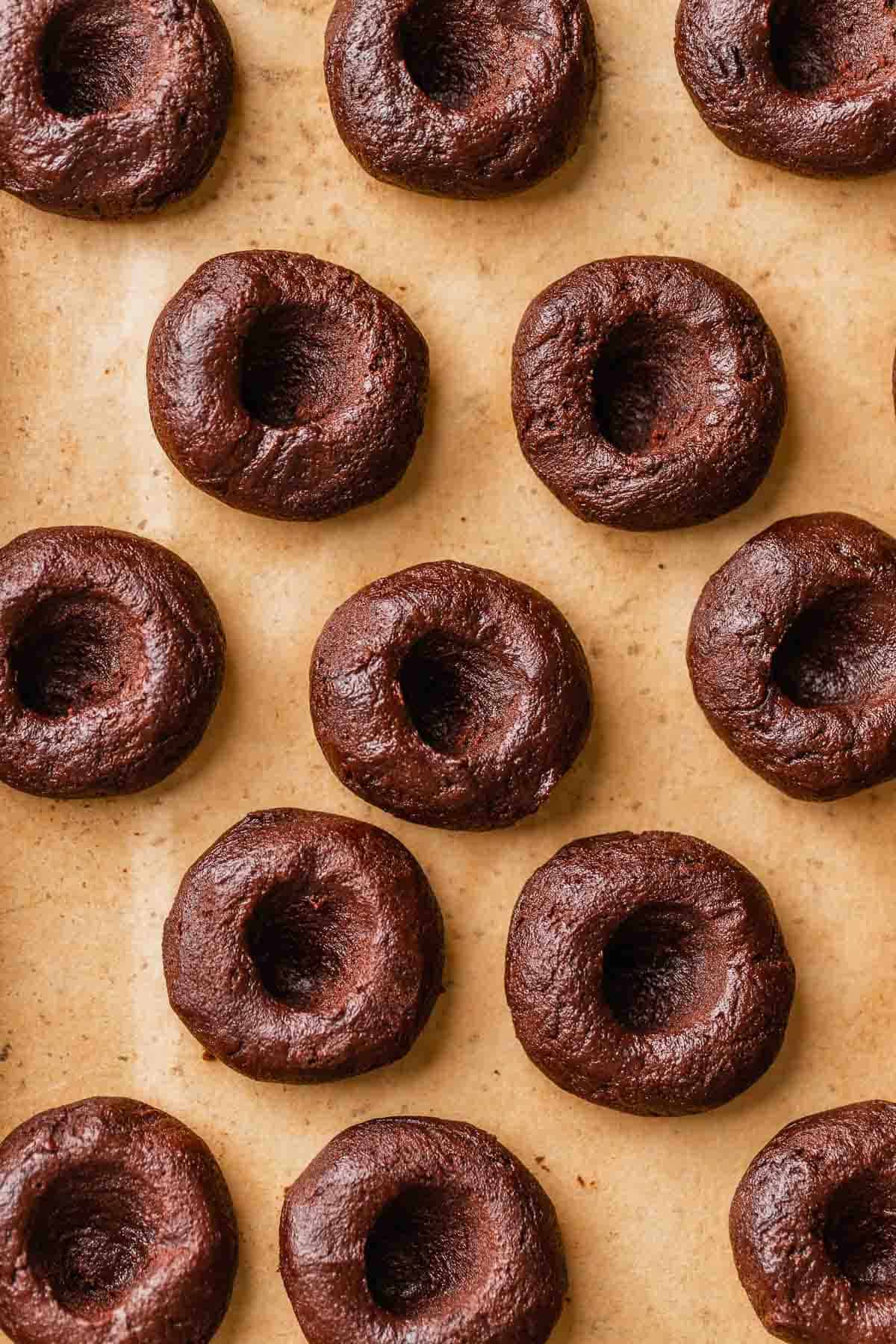 Chocolate cookie dough balls with indents in the centers on a baking tray.