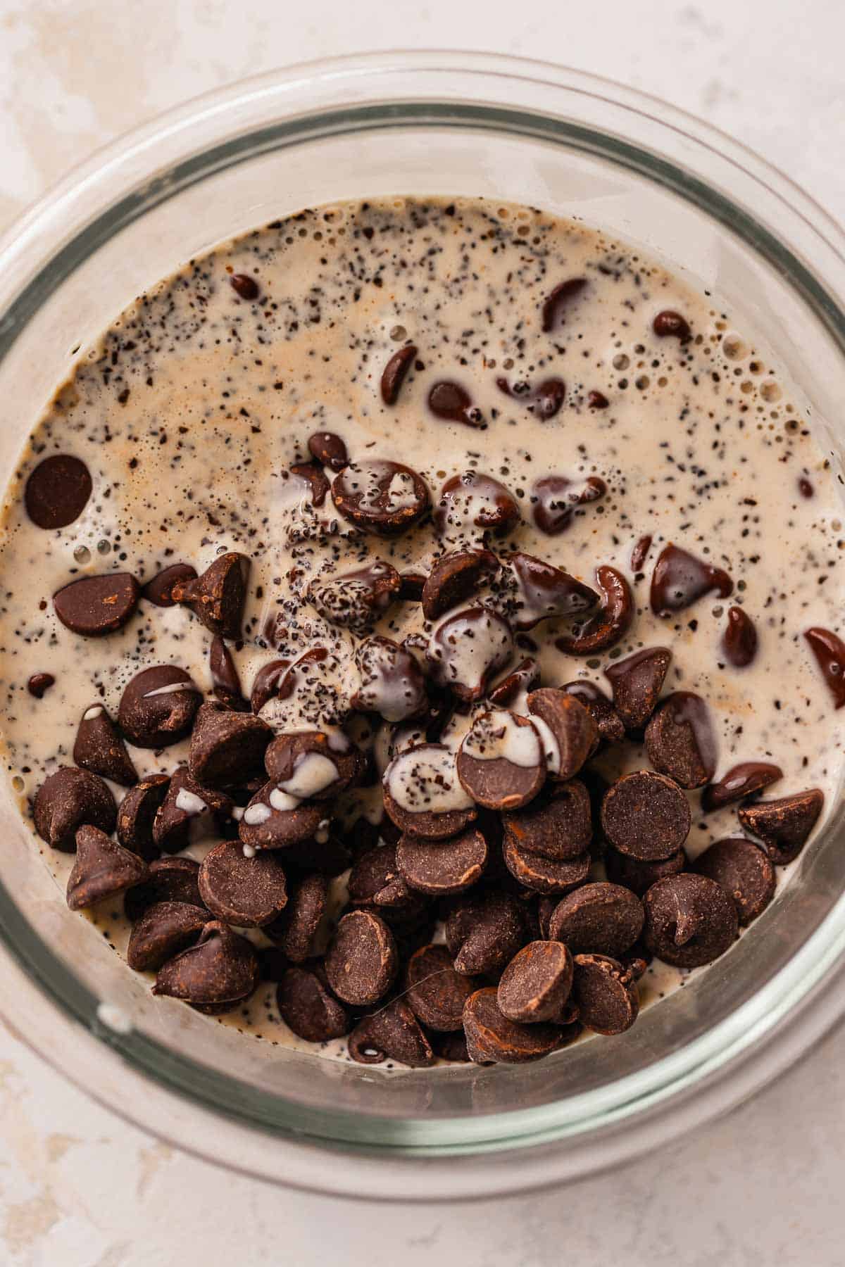 A glass bowl with chocolate chips, coffee, and heavy cream poured over the top.