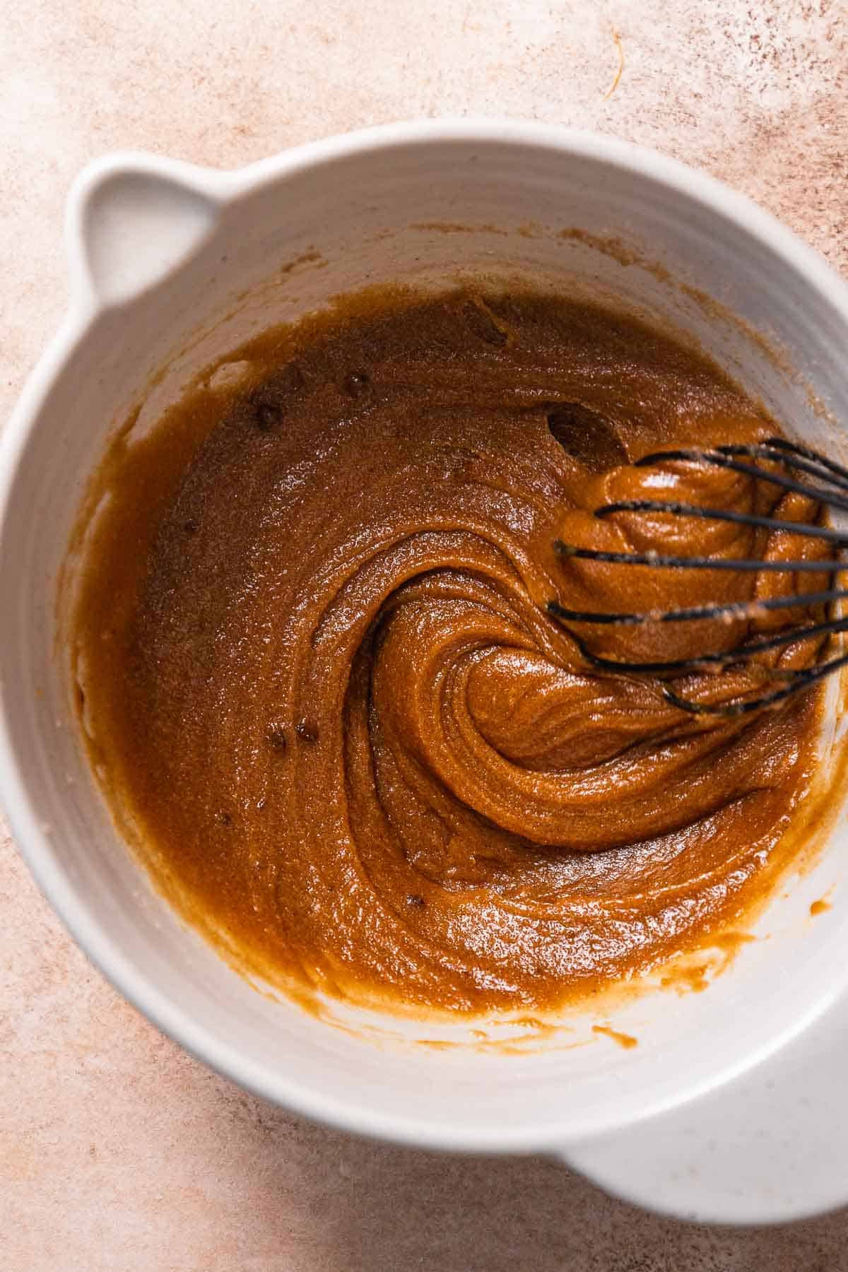 A mixing bowl with creamed butter, sugar, molasses, and egg whisked together.