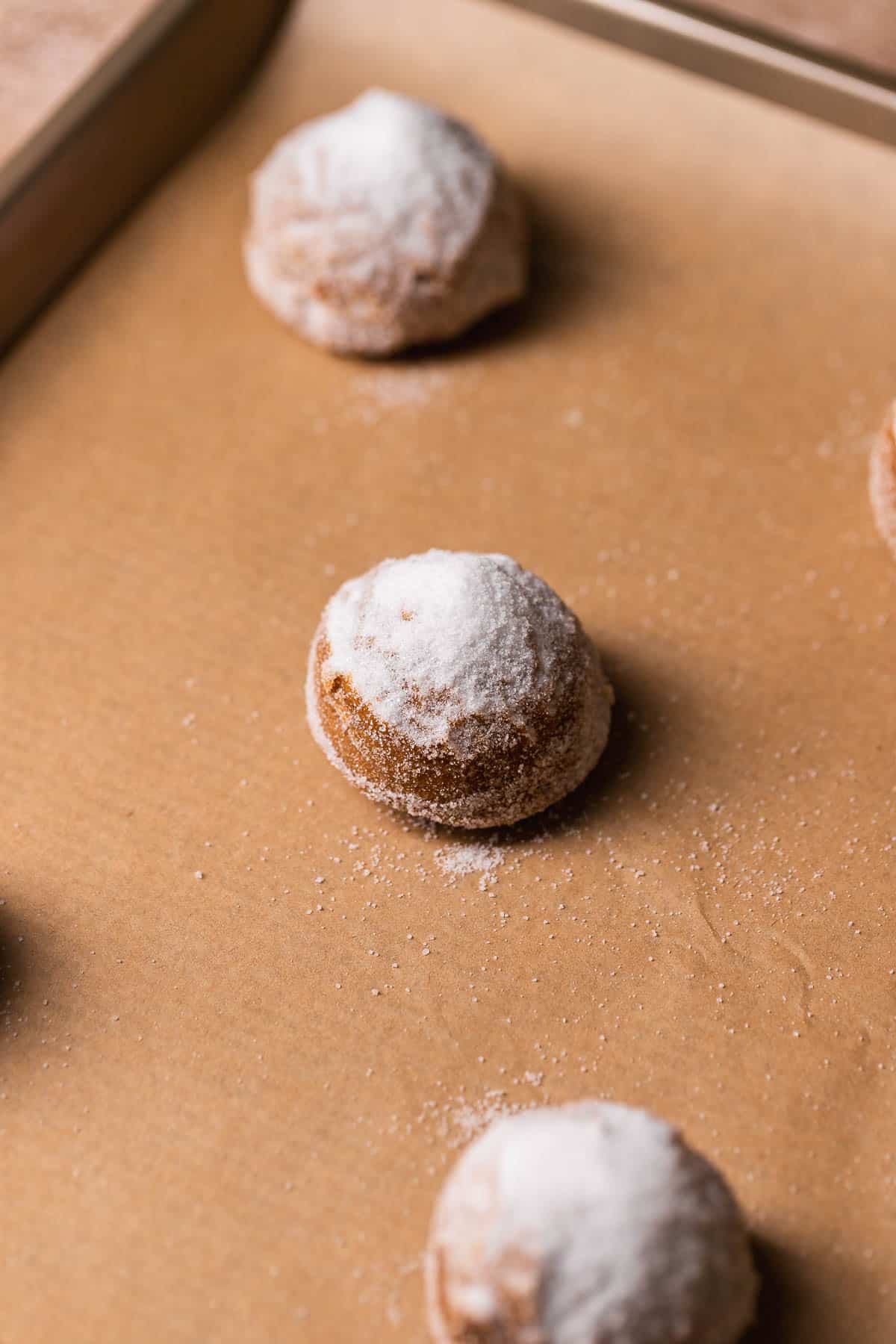 Molasses cookie dough ball on a baking sheet with a pile of white sugar on top.