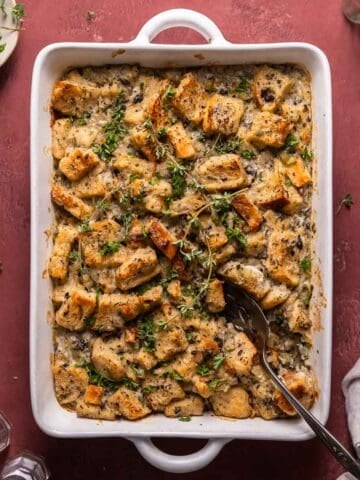 Savory bread pudding in a white baking pan with fresh thyme leaves on top.