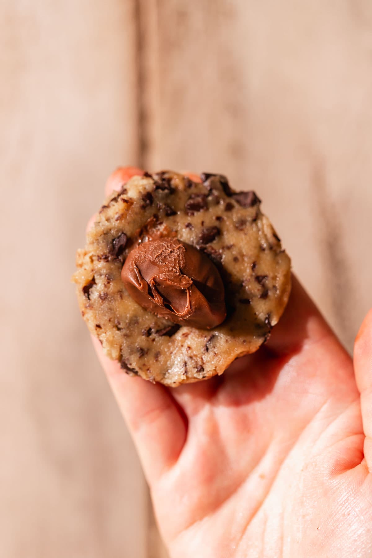 A hand holding the cookie dough that is being stuffed with chocolate.