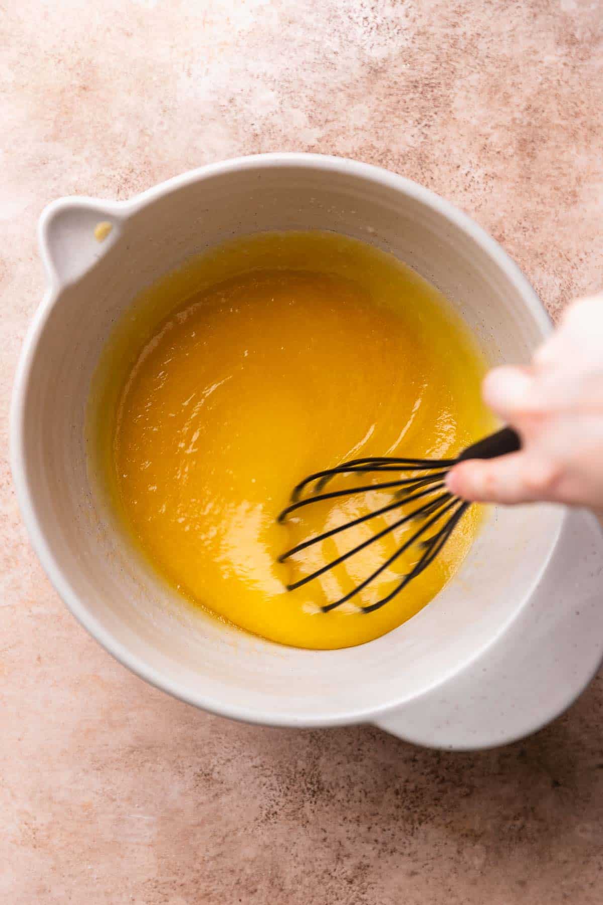 A hand whisking together the wet ingredients in a mixing bowl.