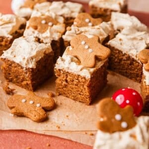 A slice of gingerbread cake on brown parchment paper with mini gingerbread cookies on top.