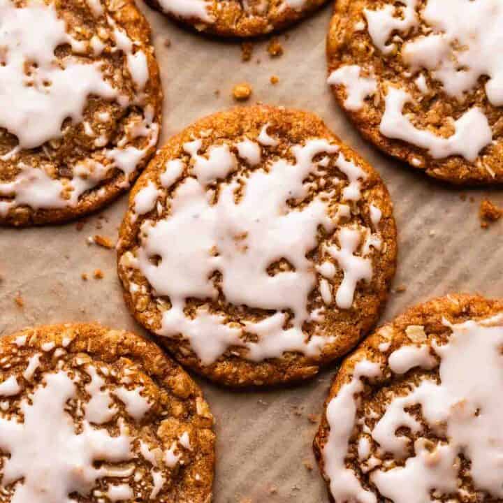 Oatmeal cookies with icing on a parchment lined baking tray.