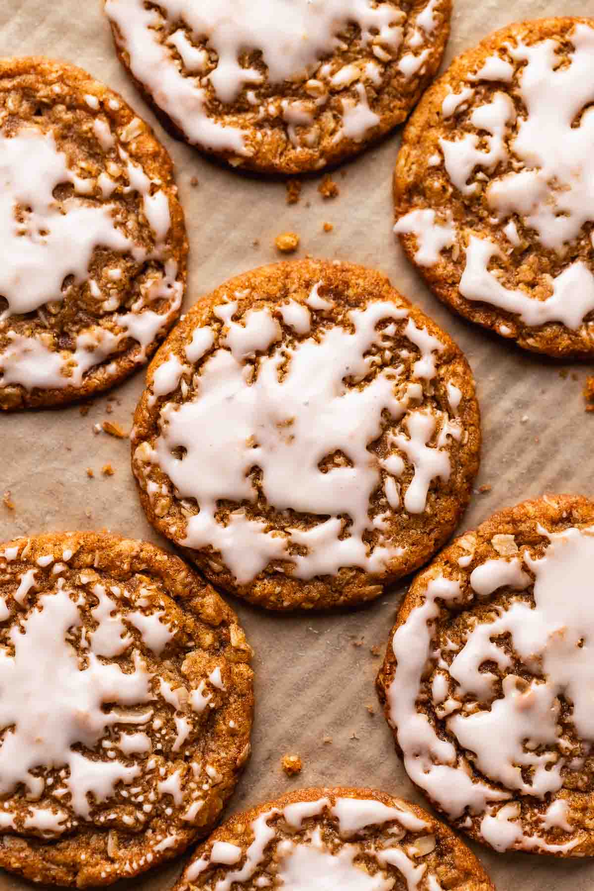 Iced oatmeal cookies on a brown parchment paper lined baking tray.