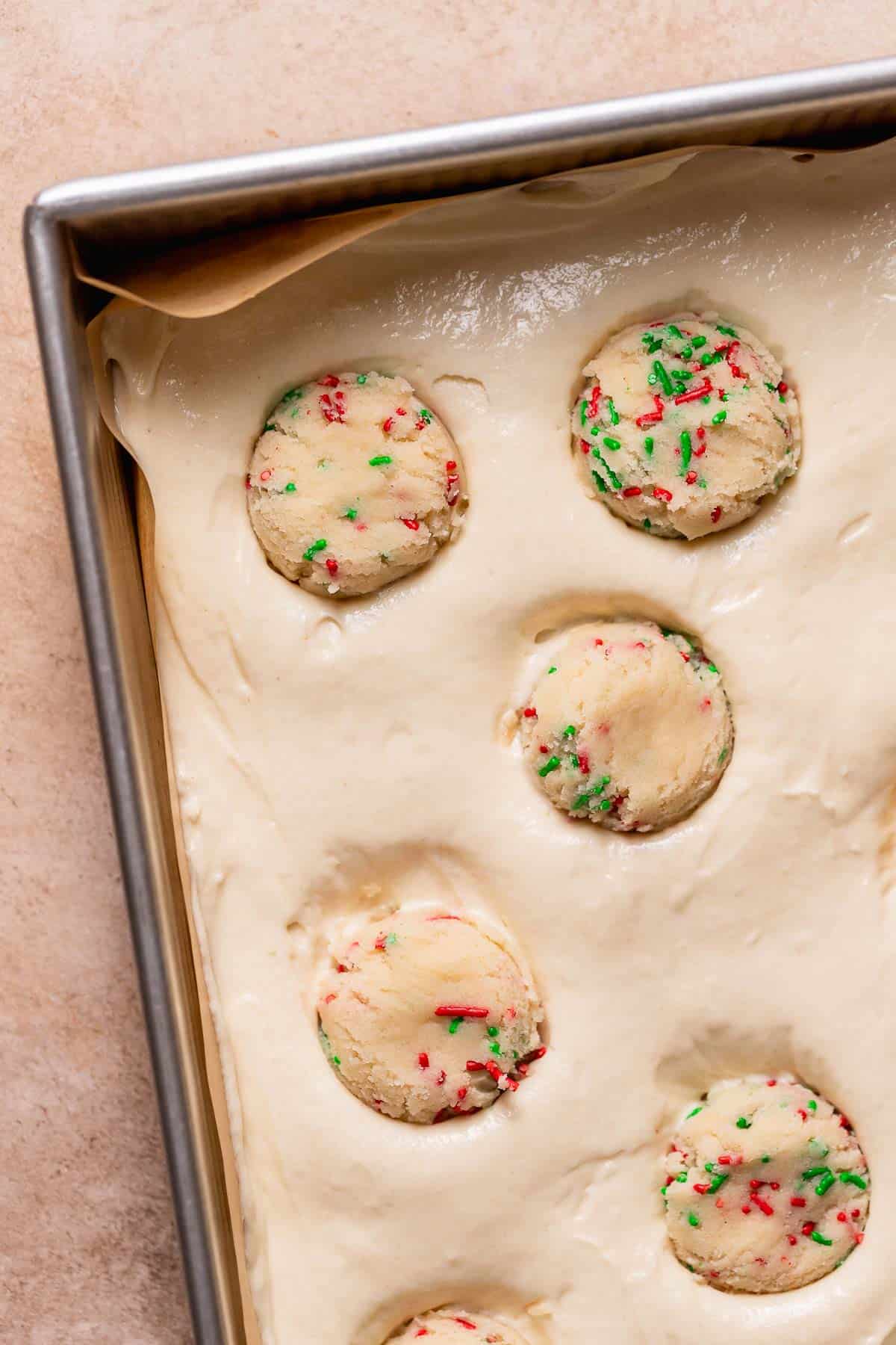 A baking pan full of vanilla cake batter with sugar cookie dough balls pressed into the top.