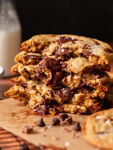 A stack of bakery style chocolate chip cookies broken in half to show the gooey centers.