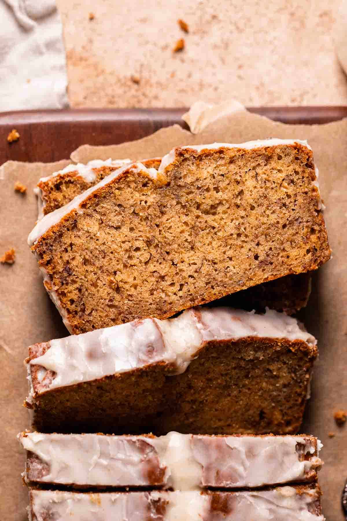 A loaf of brown butter banana bread on brown parchment paper with a slice laying flat to show the moist texture.