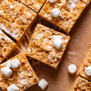 Brown butter krispie treats on brown parchment paper surrounded by mini marshmallows.