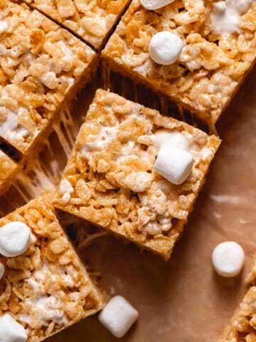 Brown butter krispie treats on brown parchment paper surrounded by mini marshmallows.