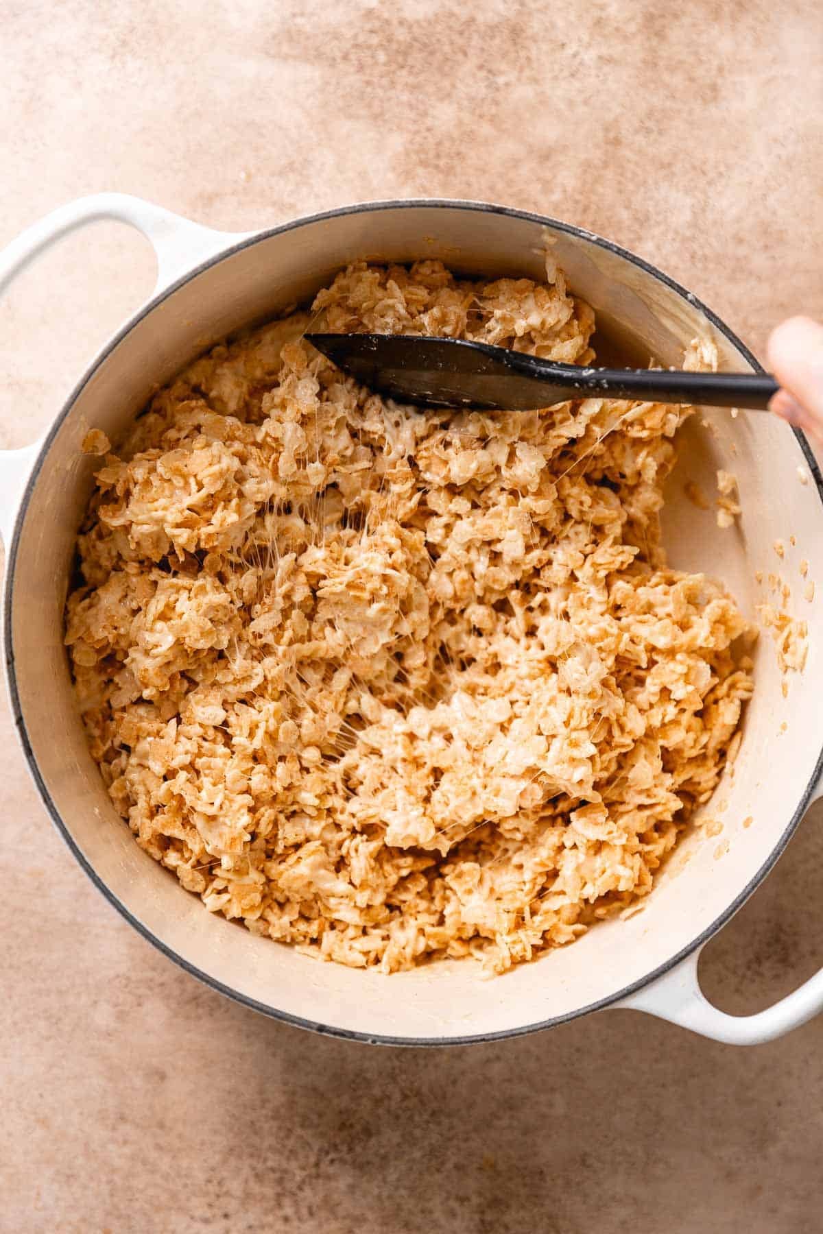 A rubber spatula folding the crispy rice cereal into the brown butter and melted marshmallow mixture.