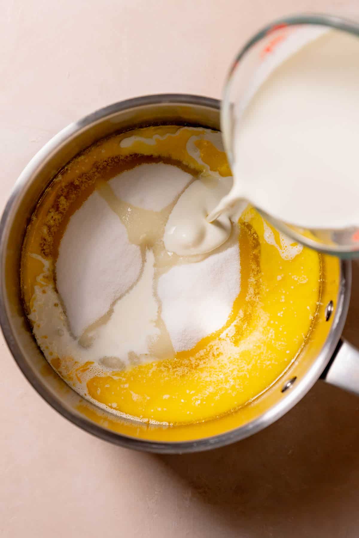 Pouring heavy cream into a pot with melted butter and sugar.