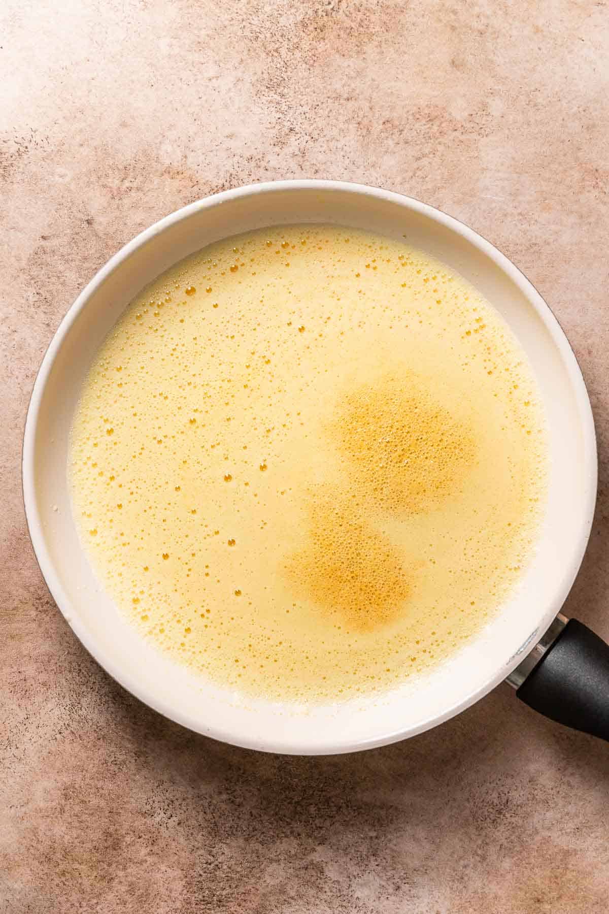A white pan with melted butter and a thick layer of foam on top.