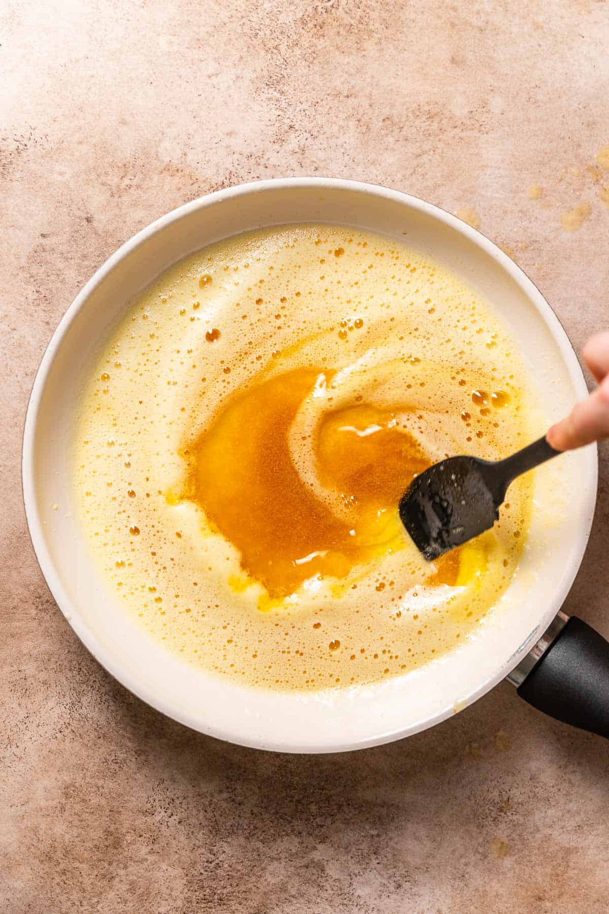 A hand stirring the melted butter in a pan to show the browned milk solids.