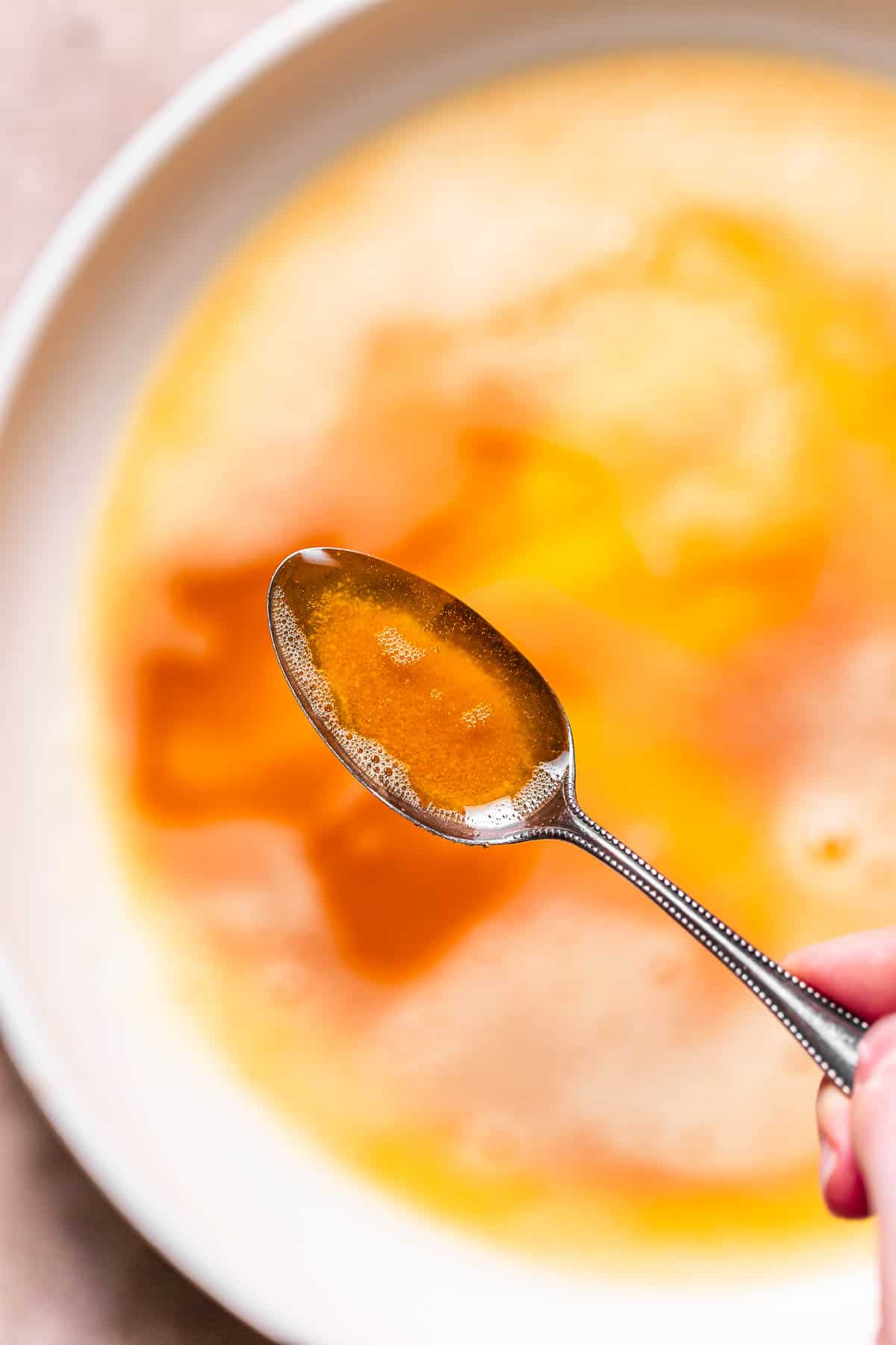 A spoon holding liquid brown butter over a pan.