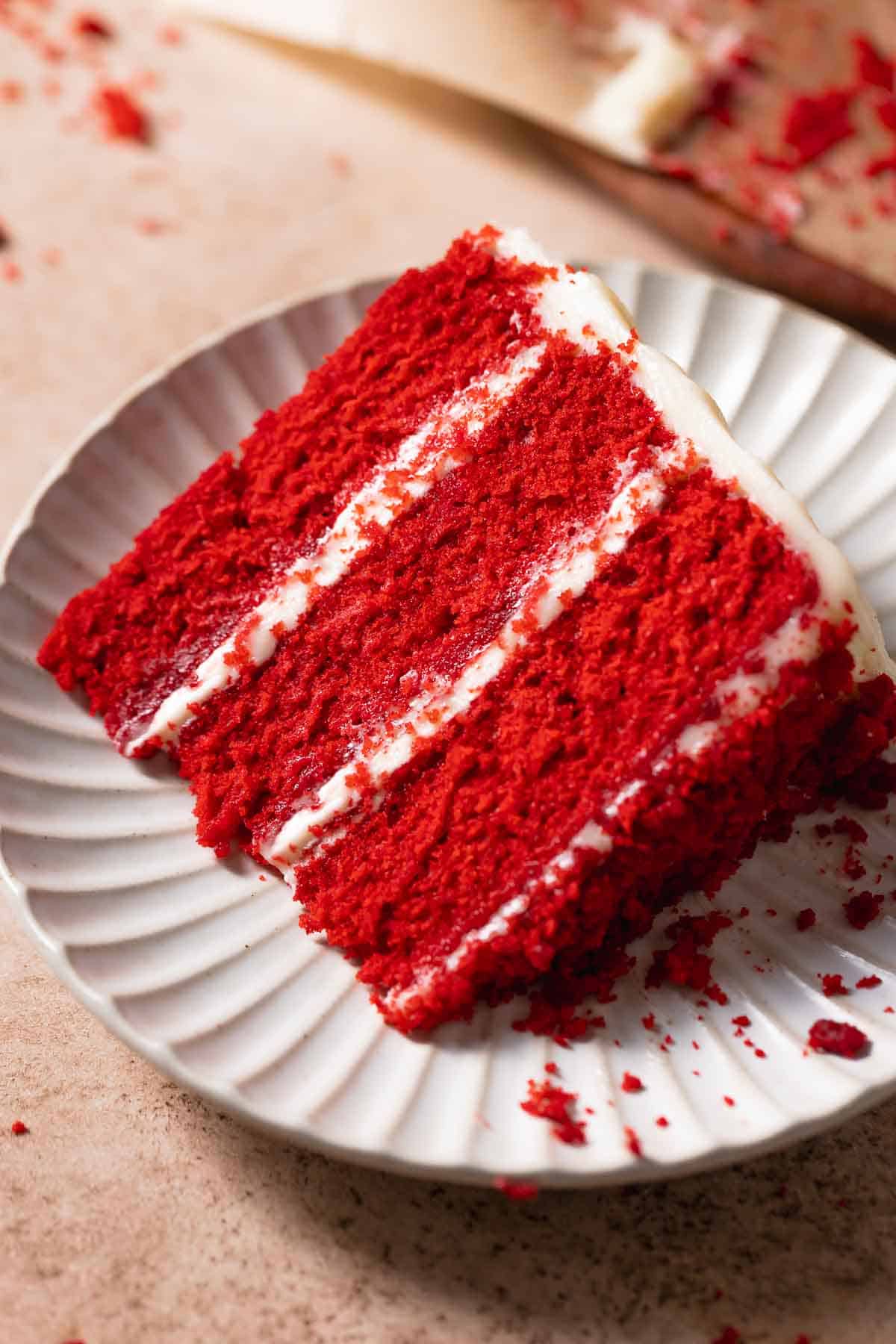 A slice of super moist red velvet cake on a white plate.