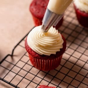Cream cheese frosting being piped on top of a cupcake.