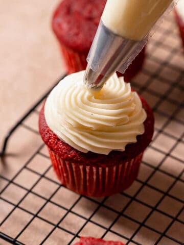 Cream cheese frosting being piped on top of a cupcake.