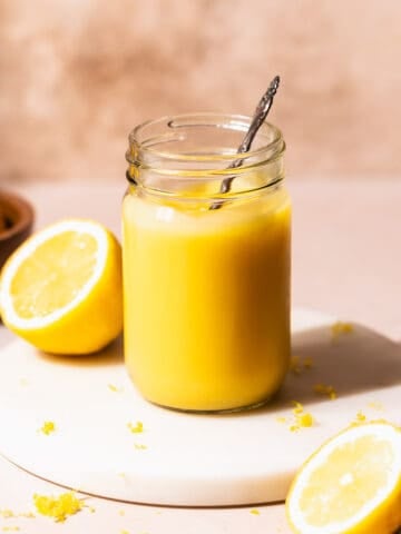 Homemade lemon curd in a glass mason jar with a spoon dipping into it.