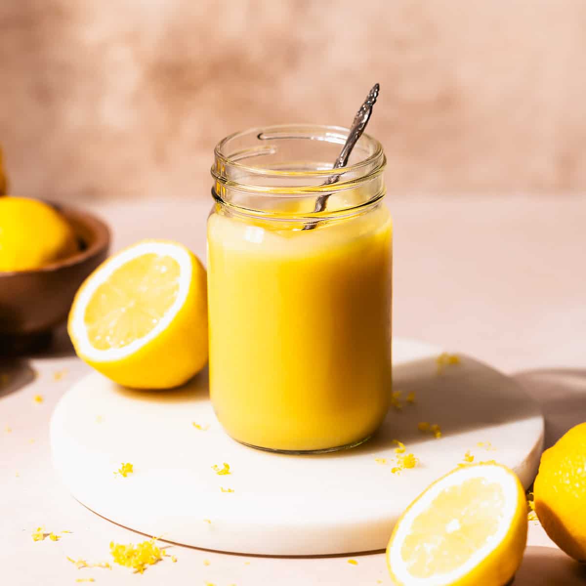 Homemade lemon curd in a glass mason jar with a spoon dipping into it.